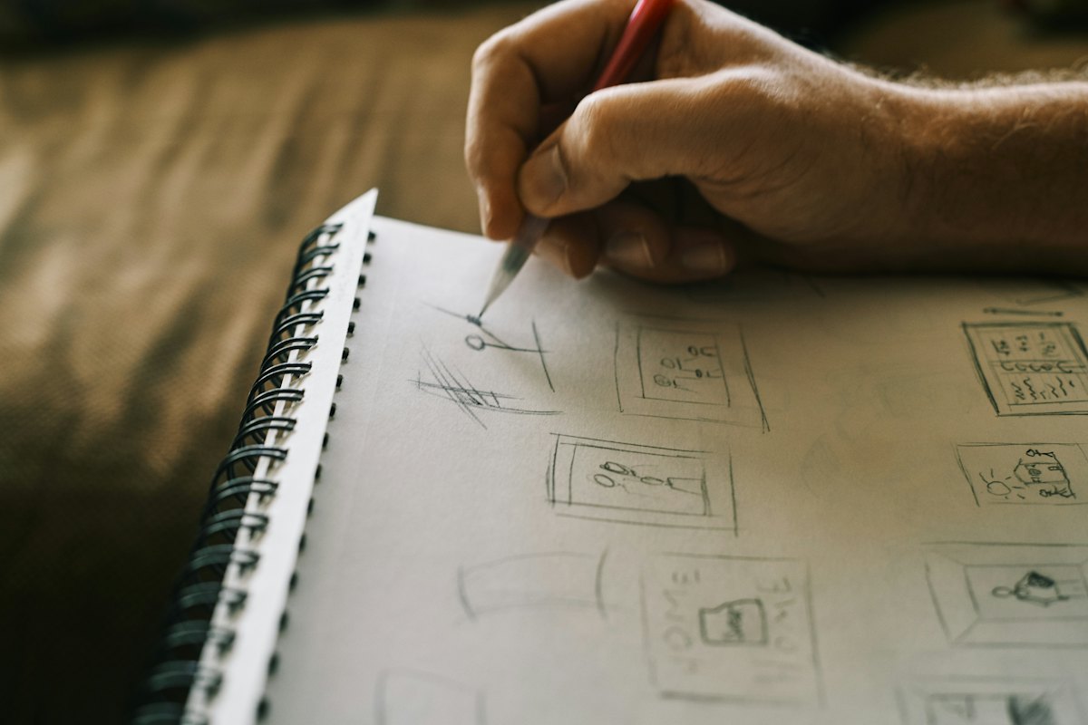 A hand sketching page layouts in a spiral notebook